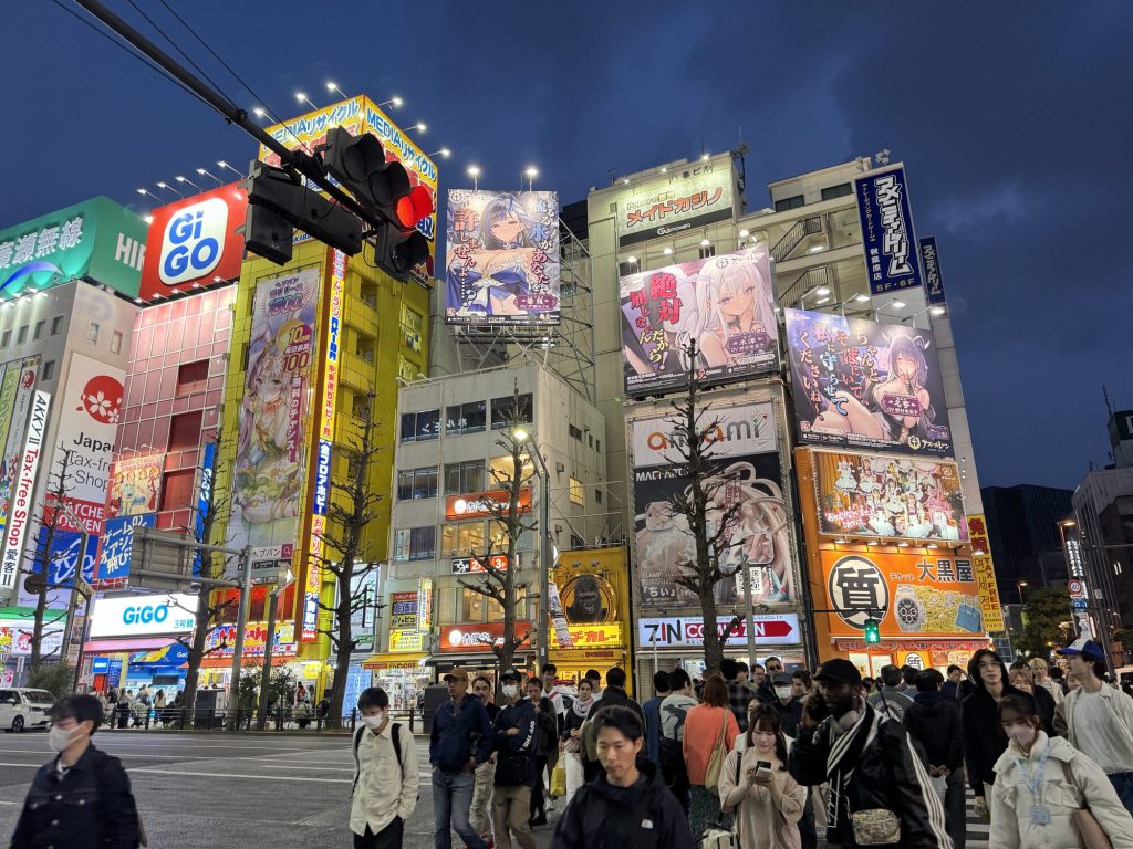 Ikoniczne skrzyżowanie Akihabary wieczorem — GiGO, anime billboardy, tłum. Ten kadr każdy kojarzy.