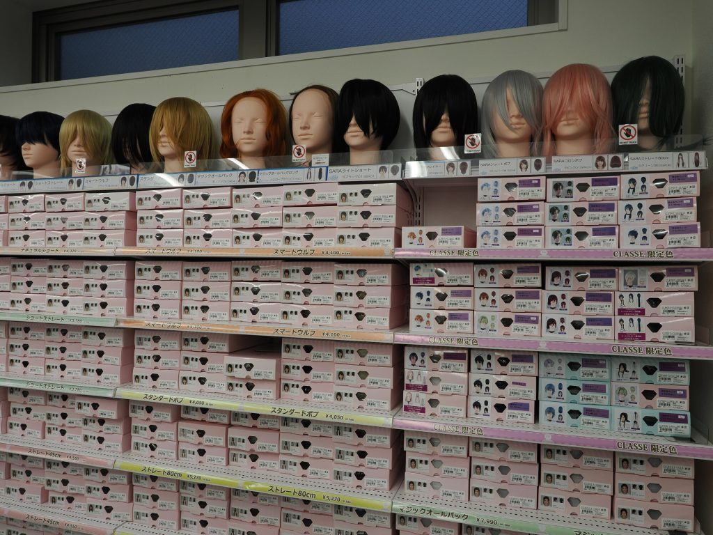 Ściana z perukami do cosplay w Animate Ikebukuro - dziesiątki kolorowych peruk w opakowaniach