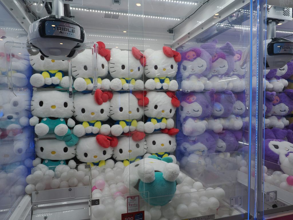 Maszyna crane game w GiGO z Hello Kitty i Kuromi - dziesiątki białych i fioletowych pluszaków ułożonych w rzędach, ramię Triple Catcher nad nimi