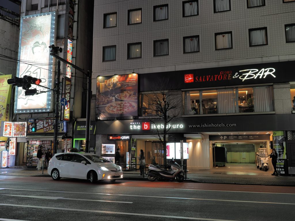 Hotel the b ikebukuro nocą - fasada z Salvatore Cuomo Bar, Toyota Prius, smok mural po lewej, wypożyczalnia skuterów
