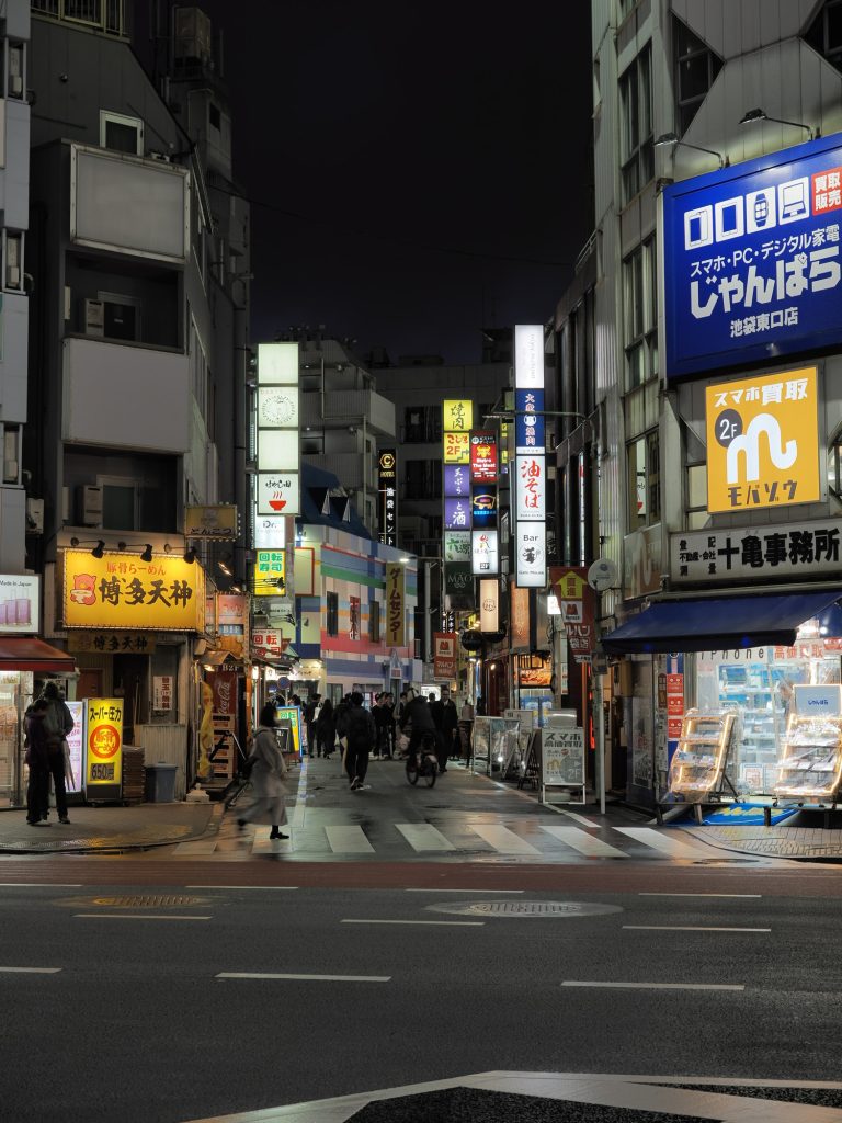 Nocna ulica wschodnie Ikebukuro - Hakata Tenjin ramen szyld żółty po lewej, じゃんぱら Janbara skupuje elektronikę po prawej, ulica z restauracjami