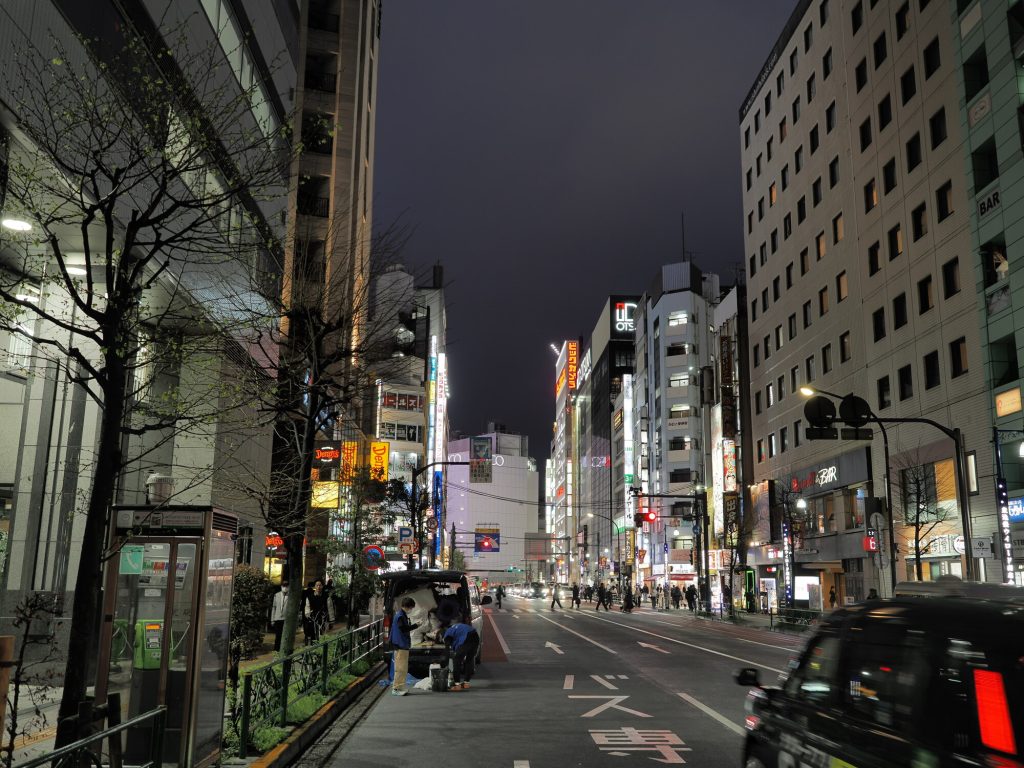 Nocna ulica Ikebukuro - riksza z rikszarzem przy chodniku, Denny's szyld w tle, OTS i Bilk Bar szyldy w perspektywie ulicy
