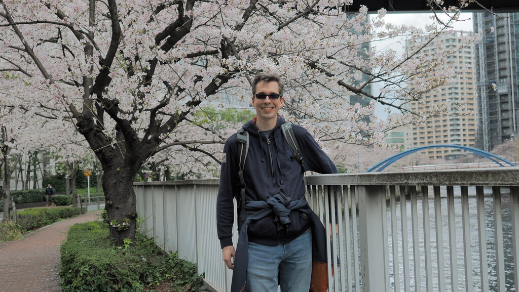 Kamil przy barierce nad kanałem z sakurą, plecak, okulary przeciwsłoneczne
