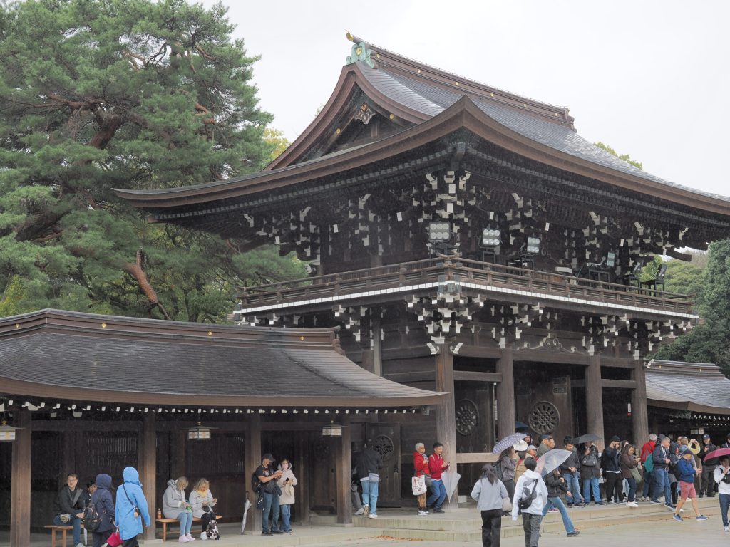 Tablica z tabliczkami ema przy Meiji Jingu, glowne sanktuarium i wielkie drzewo w tle