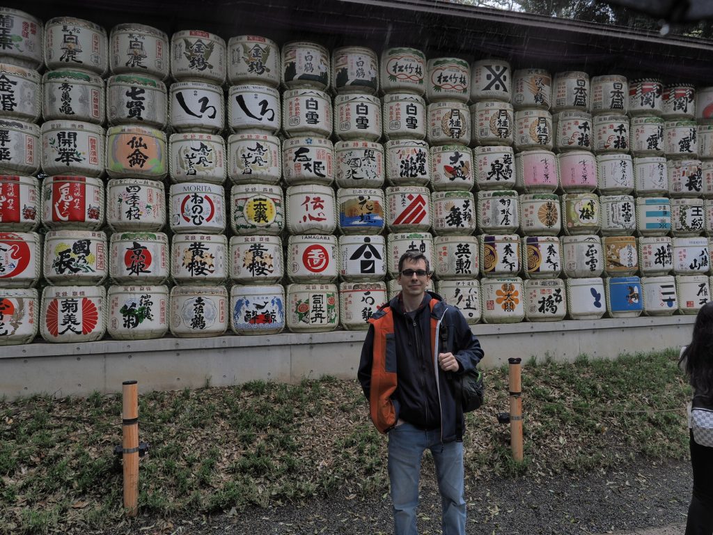 Kamil przed sciana beczolek sake w Meiji Jingu, kurtka, deszcz