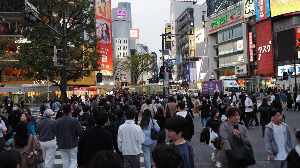 Tłum na Shibuya Crossing z wieżą Shibuya 109 i neonami GYDA w tle, zmierzch