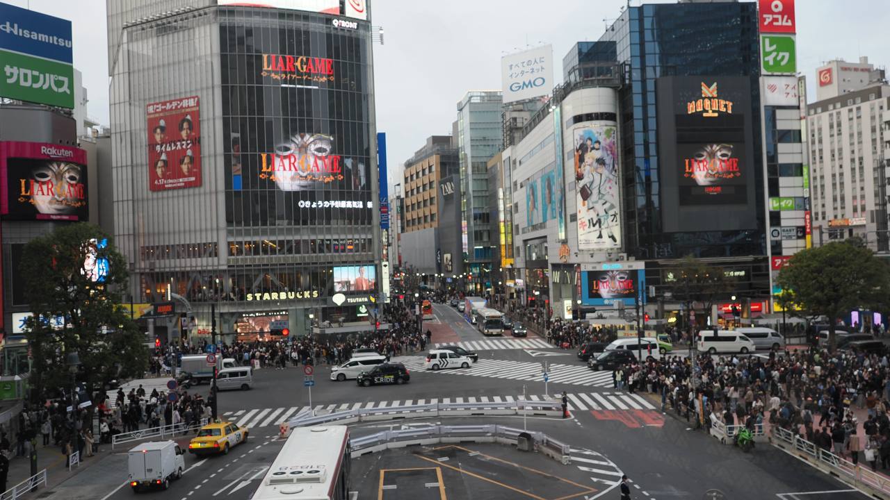 Shibuya Scramble Crossing z góry - światła czerwone, tłum czeka po wszystkich stronach, Starbucks i reklama Liar Game w tle