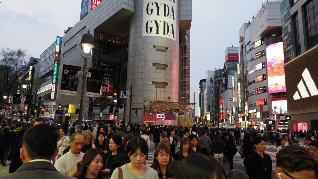 Tłum przy Shibuya Crossing z ogromnym napisem GYDA GYDA na wieżowcu, wieczór, uliczna latarnia