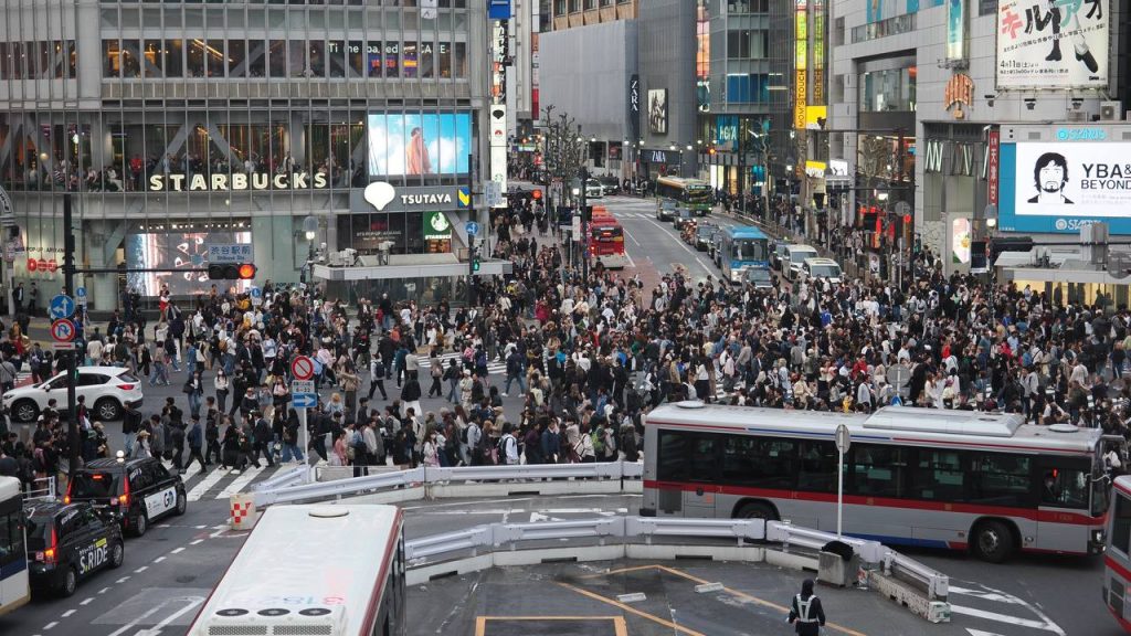 Shibuya Scramble Crossing - fala pieszych na skrzyżowaniu, setki osób w ruchu, autobusy Tokio w tle