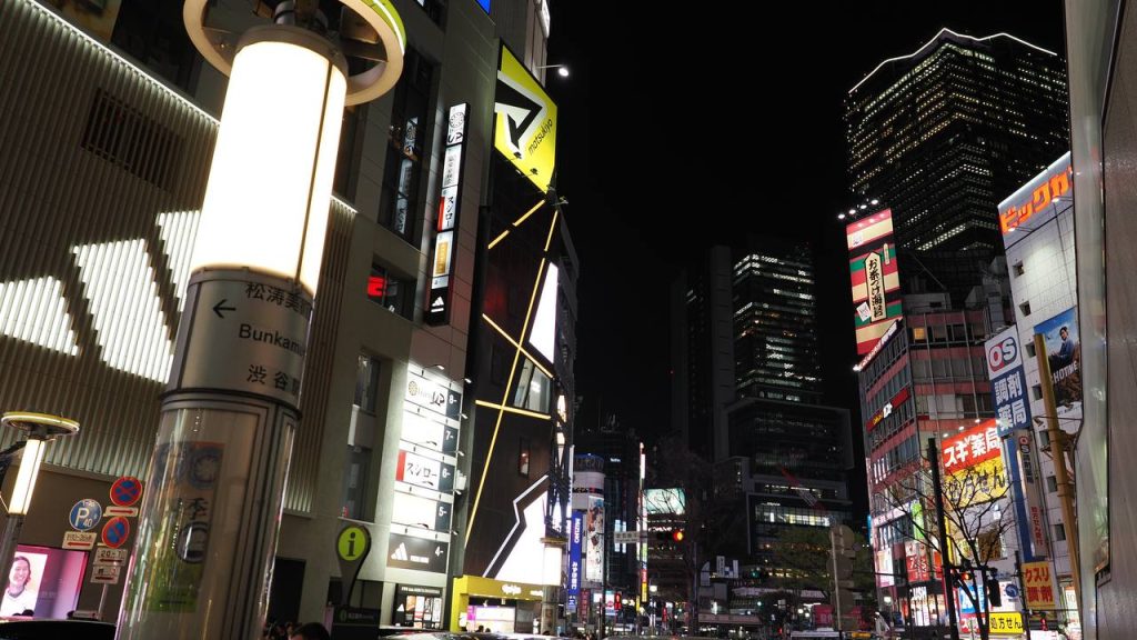 Shibuya nocą - ulica przy Bunkamura, podświetlona wieża ze strzałką Bunkamura i Matsutake Museum of Art, w tle Shibuya 109-2 i Big Camera