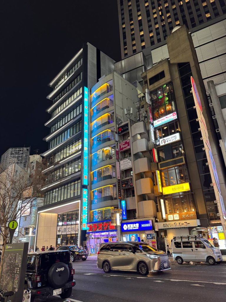 Dogenzaka nocą - wiezowiec karaoke館 z niebieskim pionowym neonem, Niku Gang, Hoang Ngam, ruch uliczny