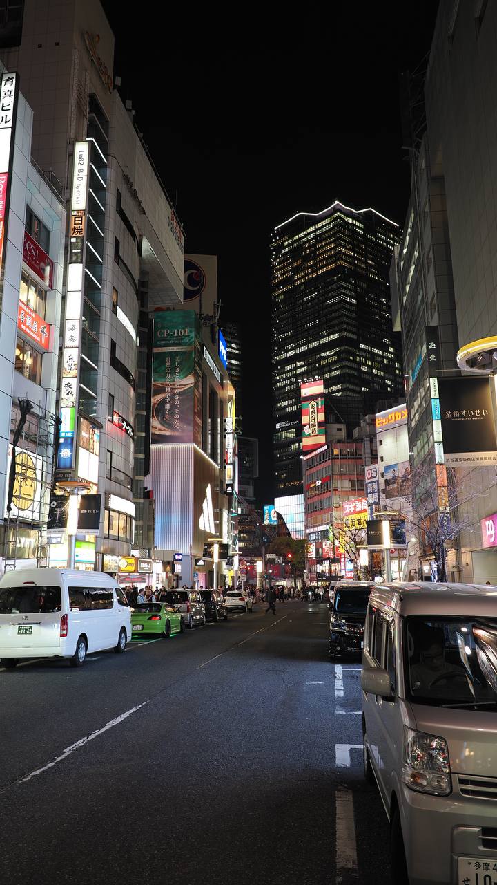 Nocna ulica Shibuya z drapaaczami chmur, CP-10F billboard kosmetyczny, zielona taksówka, Big Camera w tle