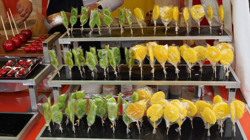 Kandyzowane kiwi i ananasy na patyku w celofanowych opakowaniach na stoisku festiwalowym