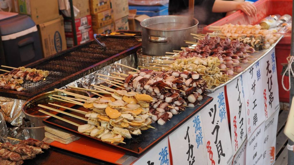 Stoisko z owocami morza na patyku - ośmiornica, krewetki, małże turban, tabliczki z cenami po japońsku