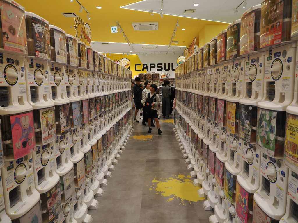 Wnętrze Capsule Lab by Capcom - rzędy gacha maszyn z obu stron korytarza, Pokémon szyldy na ścianie