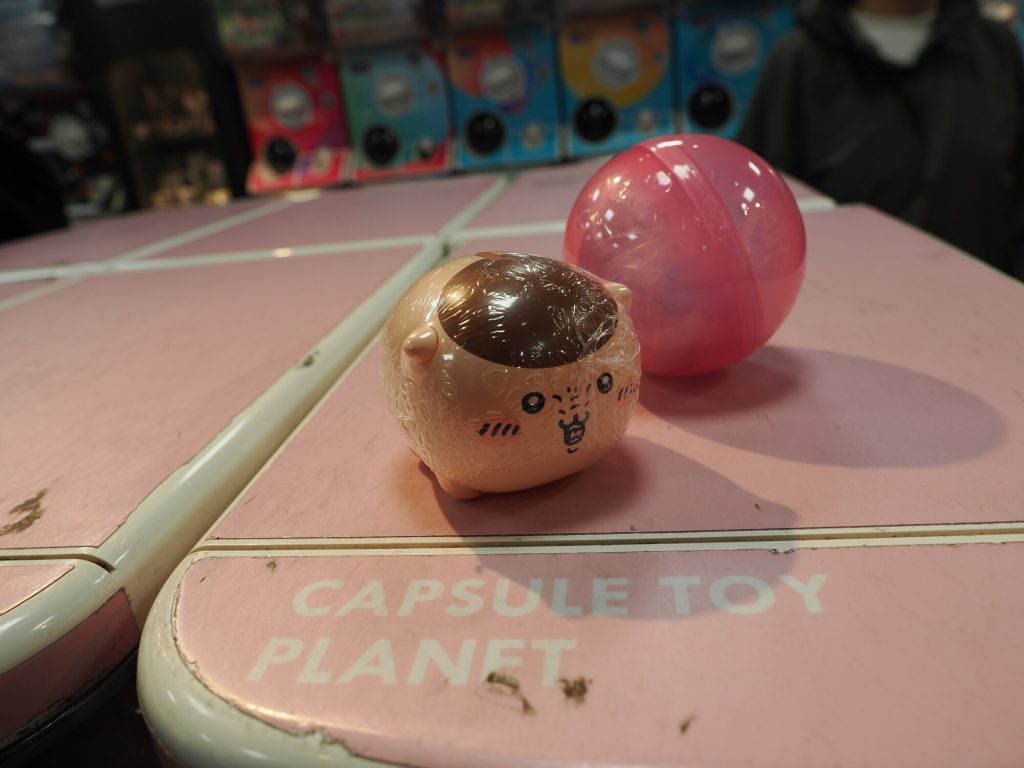 Wylosowana figurka z gacha maszyny - okrągły kotek kawaii na blacie Capsule Toy Planet, różowa kapsuła obok