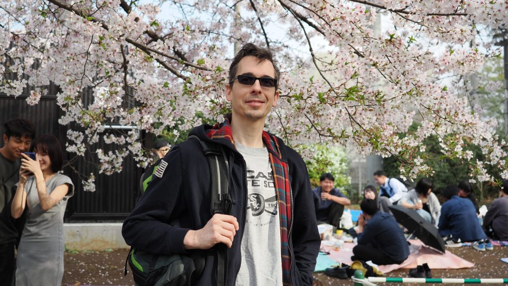 Kamil pod kwitnącą wiśnią w Parku Ueno, w tle piknikujące grupy
