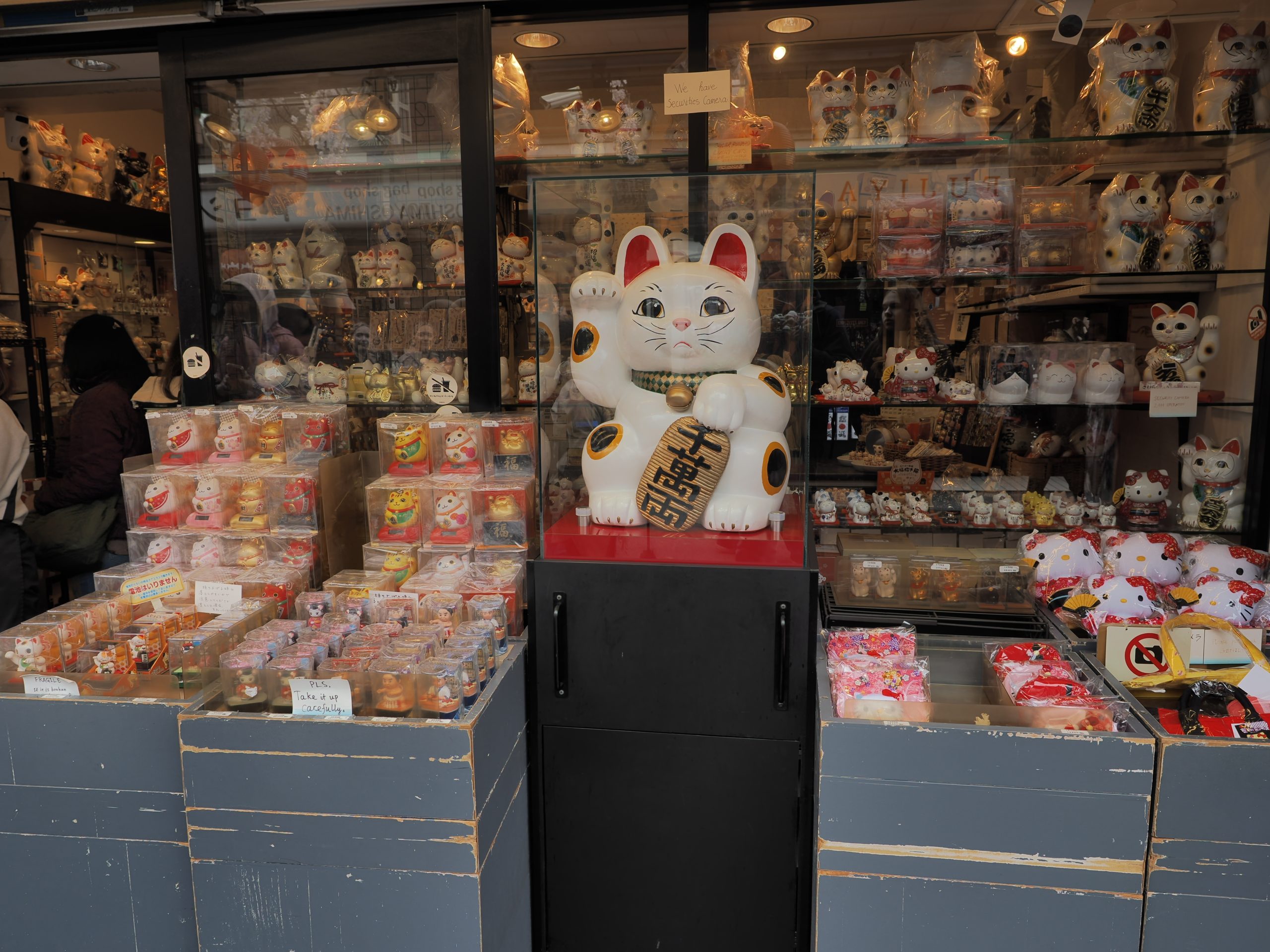 Sklep pełen figurek maneki-neko (machający kot szczęścia), setki kotów na półkach, duży kot w centrum