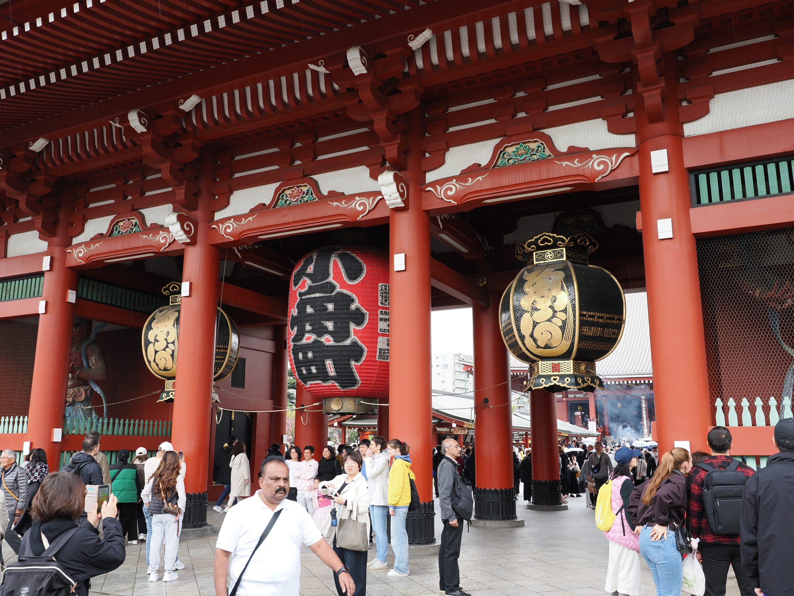 Przejście przez bramę Hozomon świątyni Senso-ji od wewnątrz: trzy wielkie latarnie, czerwone filary, tłum w przejściu, dym kadzidła w tle