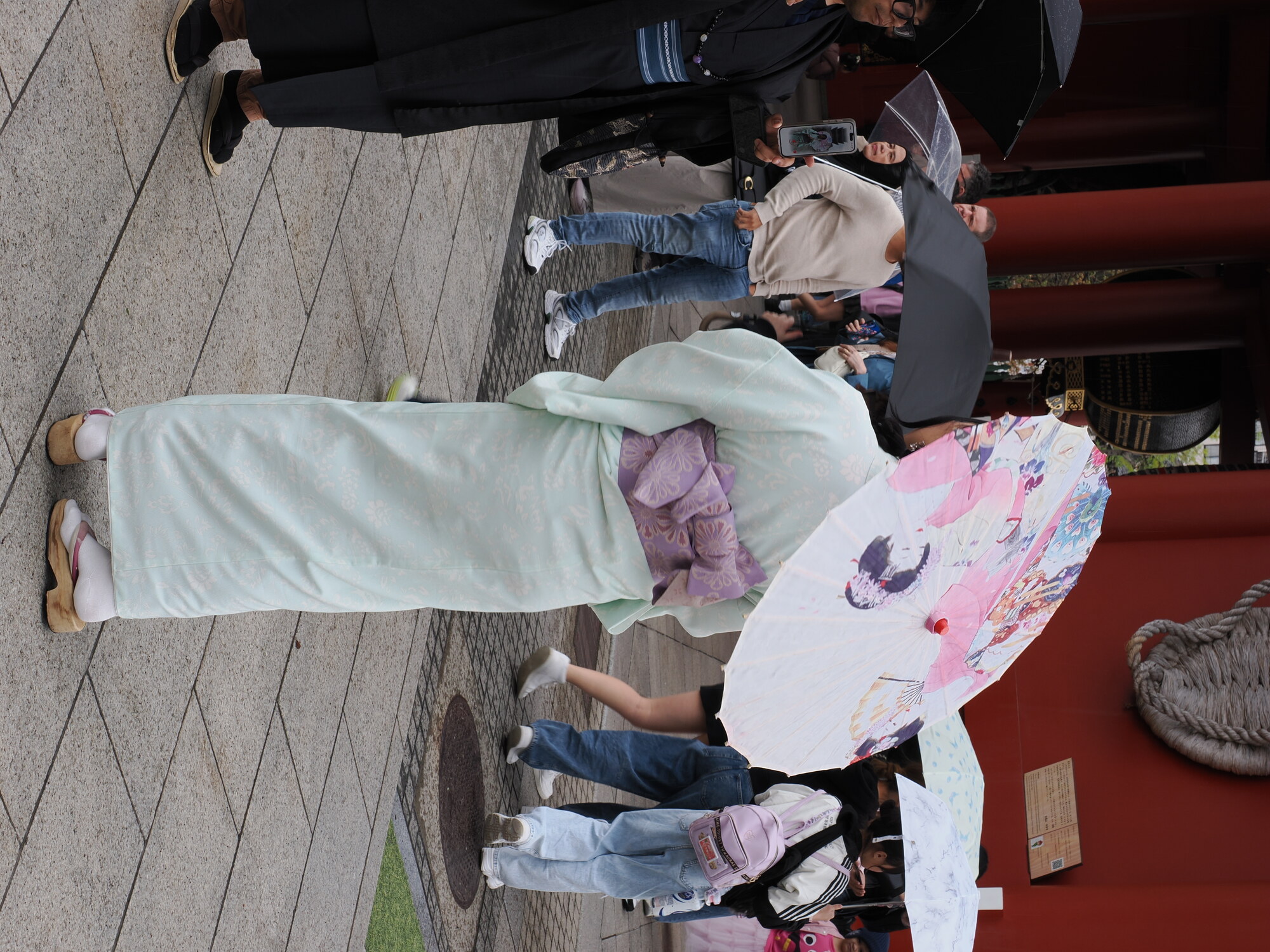 Kobieta w jasnozielonym kimono z papierową parasolką przy bramie Senso-ji