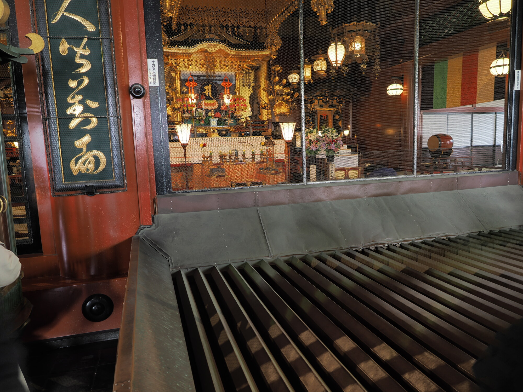 Wnętrze głównej hali świątyni Senso-ji przez kratę — złoty ołtarz buddyjski z figurką Kannon