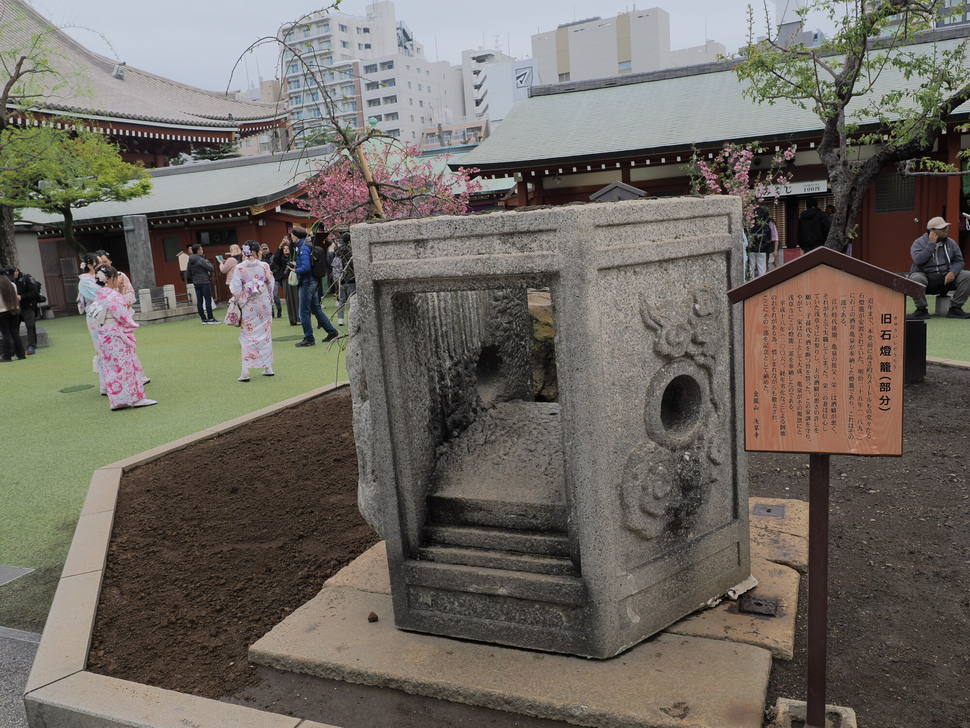 Stary kamienny lampion na dziedzińcu Senso-ji, kobiety w kolorowych yukatach w tle