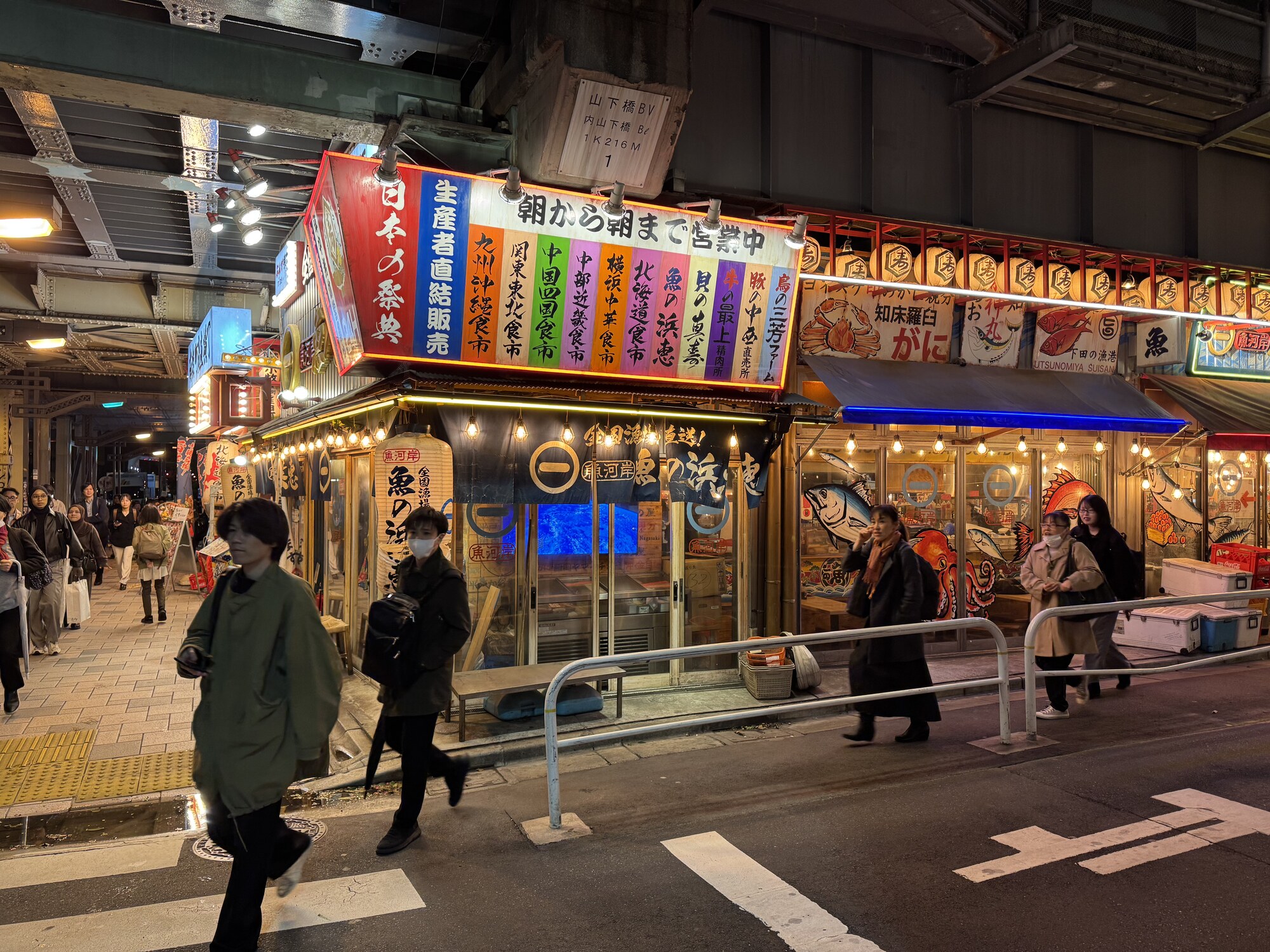 Nocna uliczka z knajpkami pod wiaduktem kolejowym, szyldy z owocami morza z całej Japonii