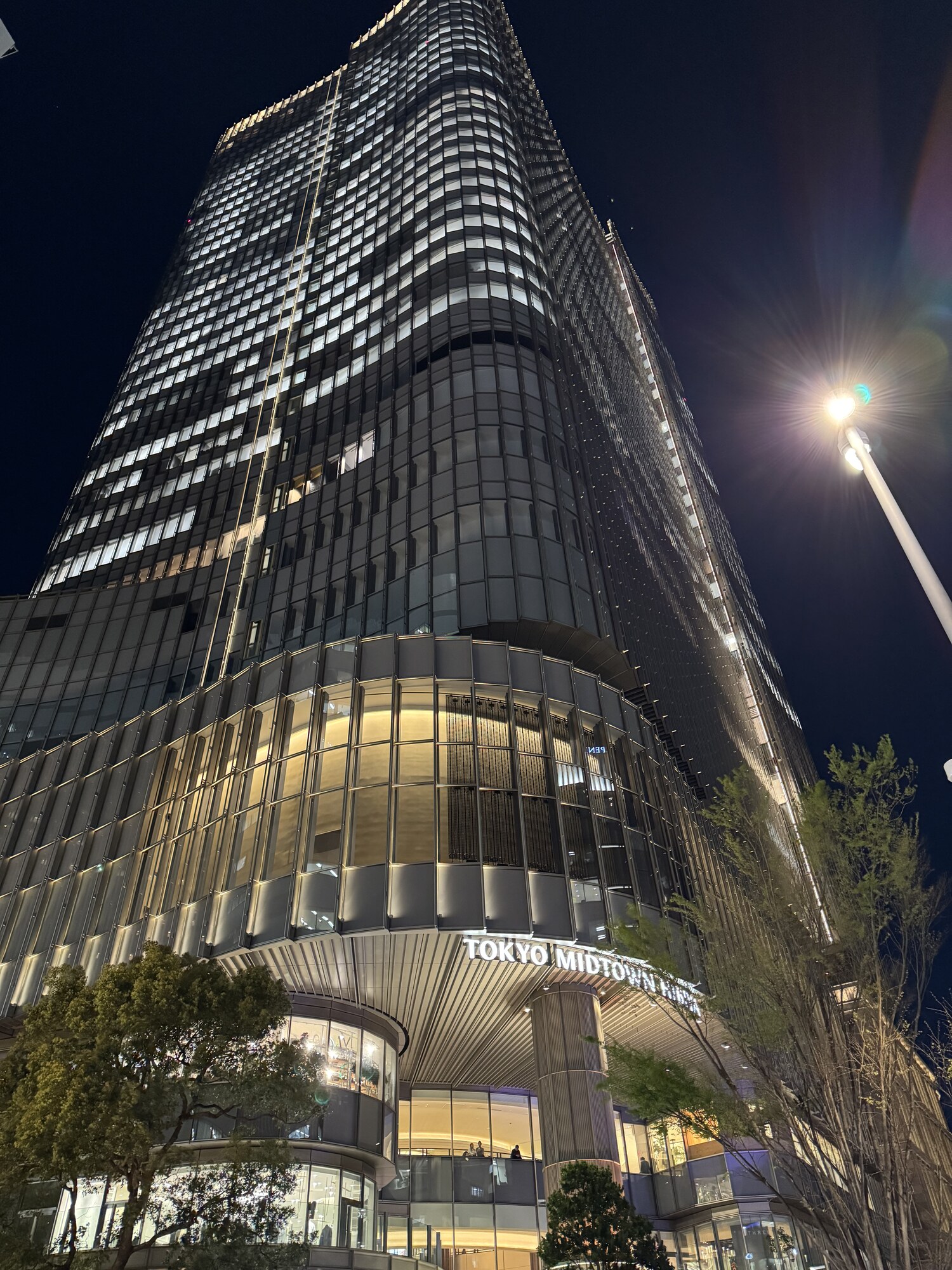 Wieżowiec Tokyo Midtown sfotografowany nocą od dołu, szklana fasada i napis Tokyo Midtown