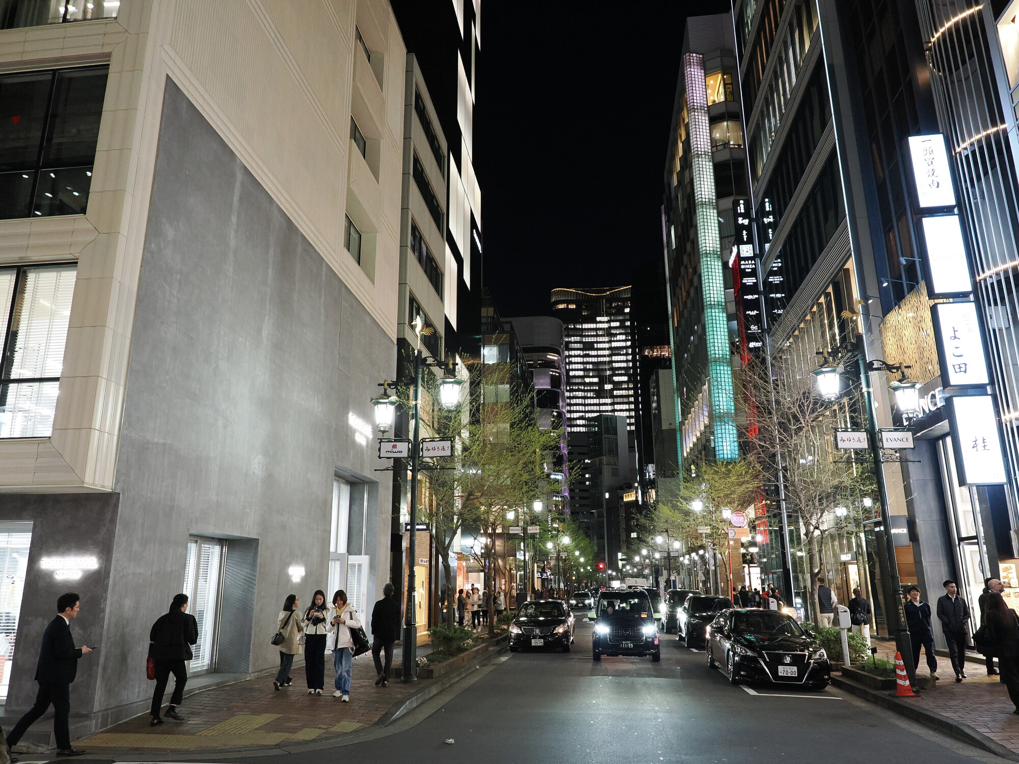 Nocna ulica Ginzy z wieżowcami w tle, auta i przechodnie, latarnie uliczne