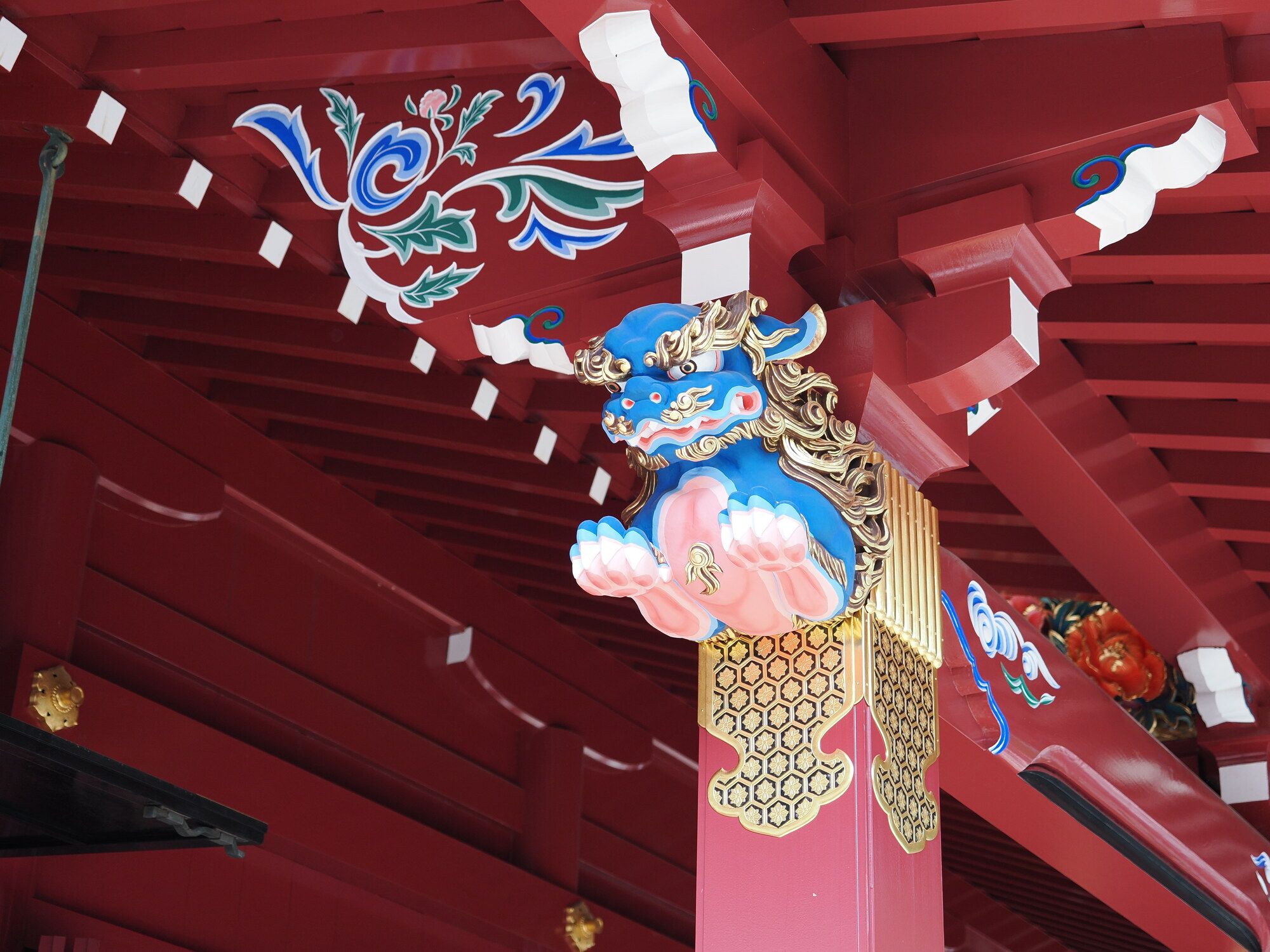 Niebieski koma-inu pod okapem wejścia do Hakone Jinja, złote zdobienia i malunki kwiatowe