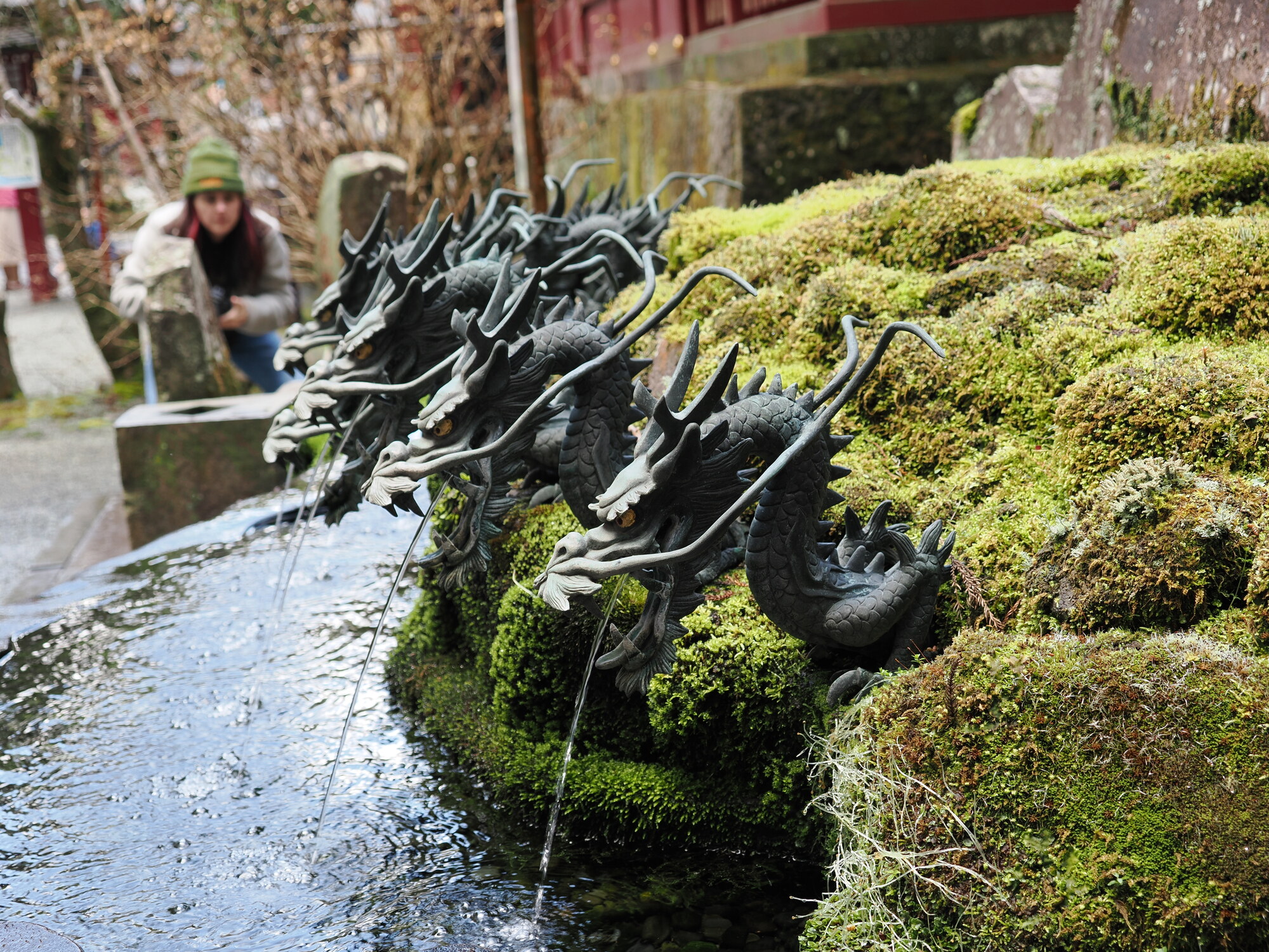 Fontanna z dziewięcioma głowami smoka plującymi wodą przy Hakone Jinja, turystka fotografuje