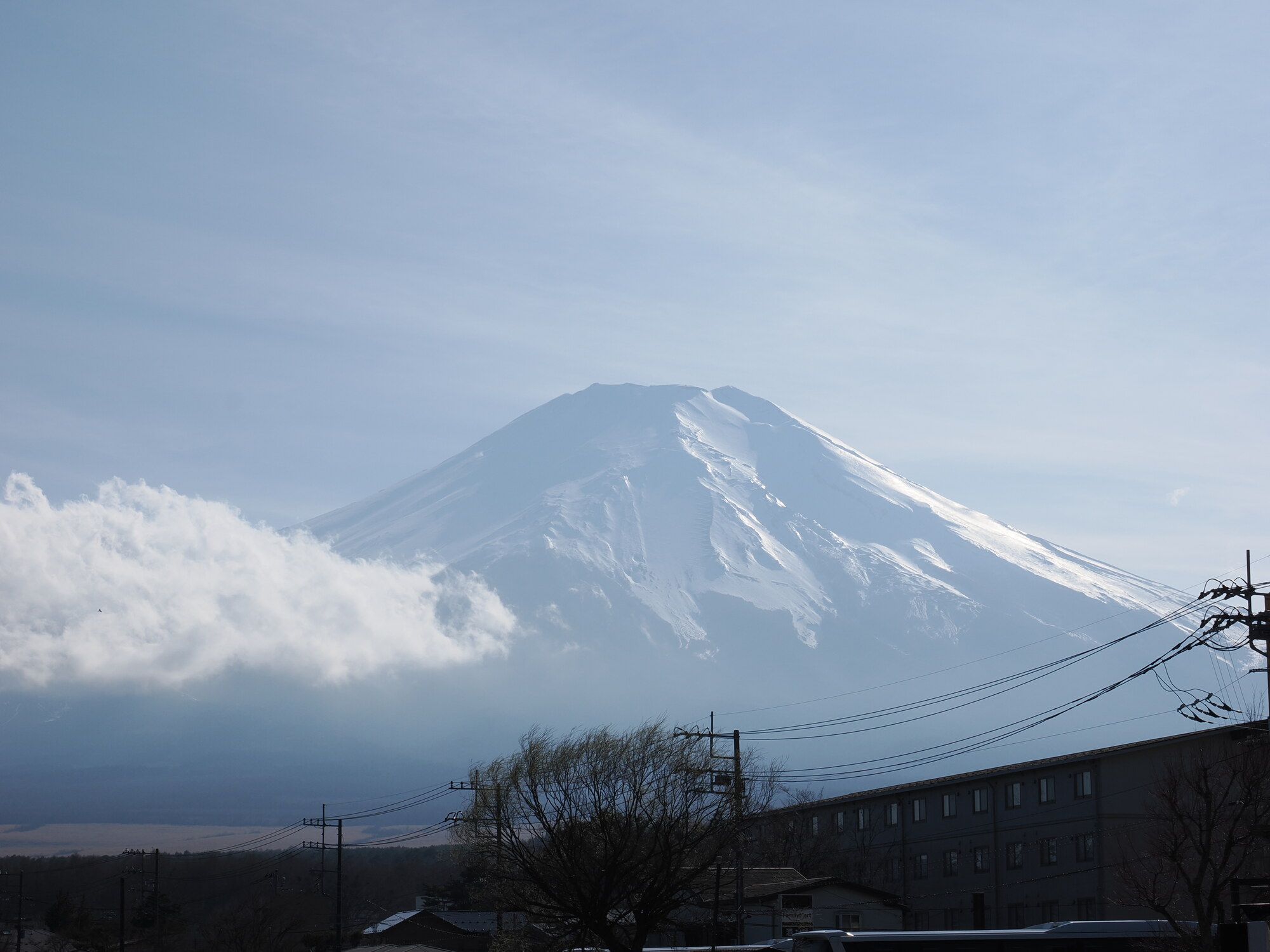 Góra Fuji wyłaniająca się nad chmurami i dachami Kawaguchiko, biały śnieg na stożku
