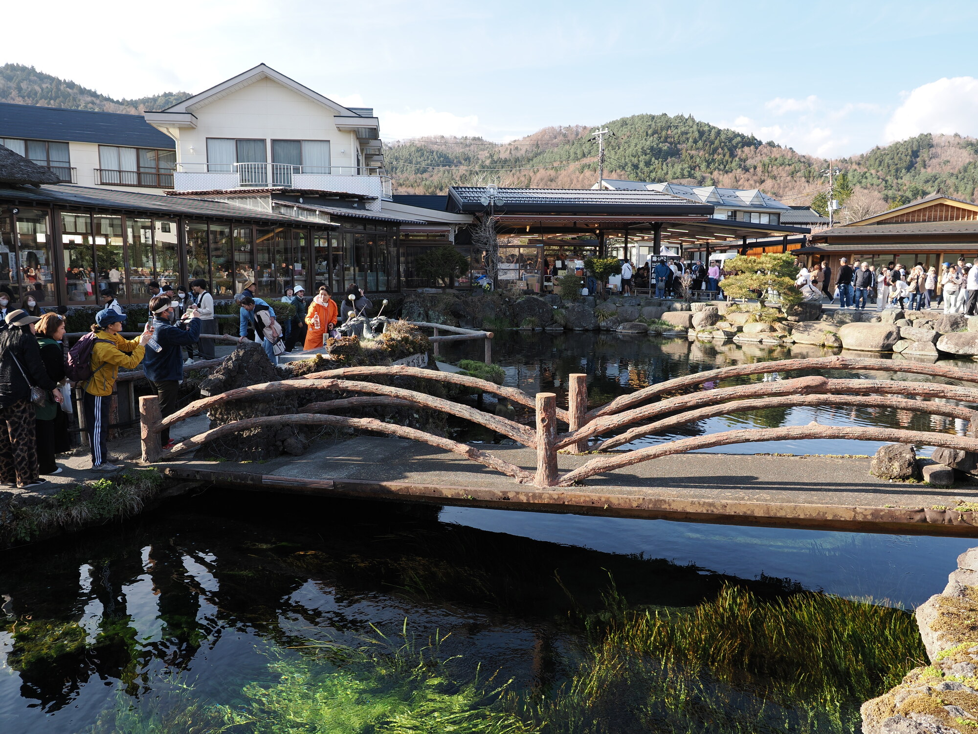 Drewniany mostek i stawy z krystalicznie czystą wodą w Oshino Hakkai, tłum przy zabytkowym domu