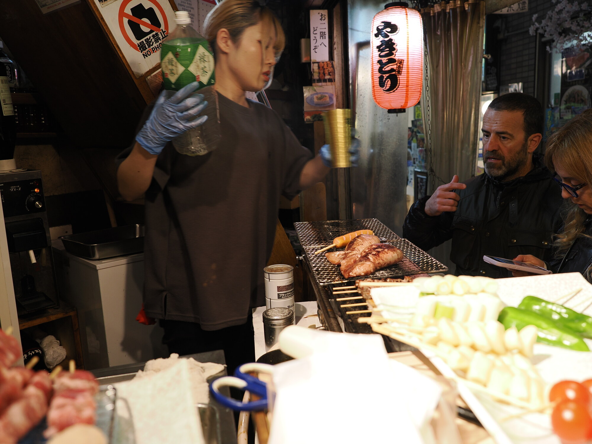 Yakitoriya w Omoide Yokocho — kucharz z butelką sosu, grill z kurczakiem, lampion yakitori i goście