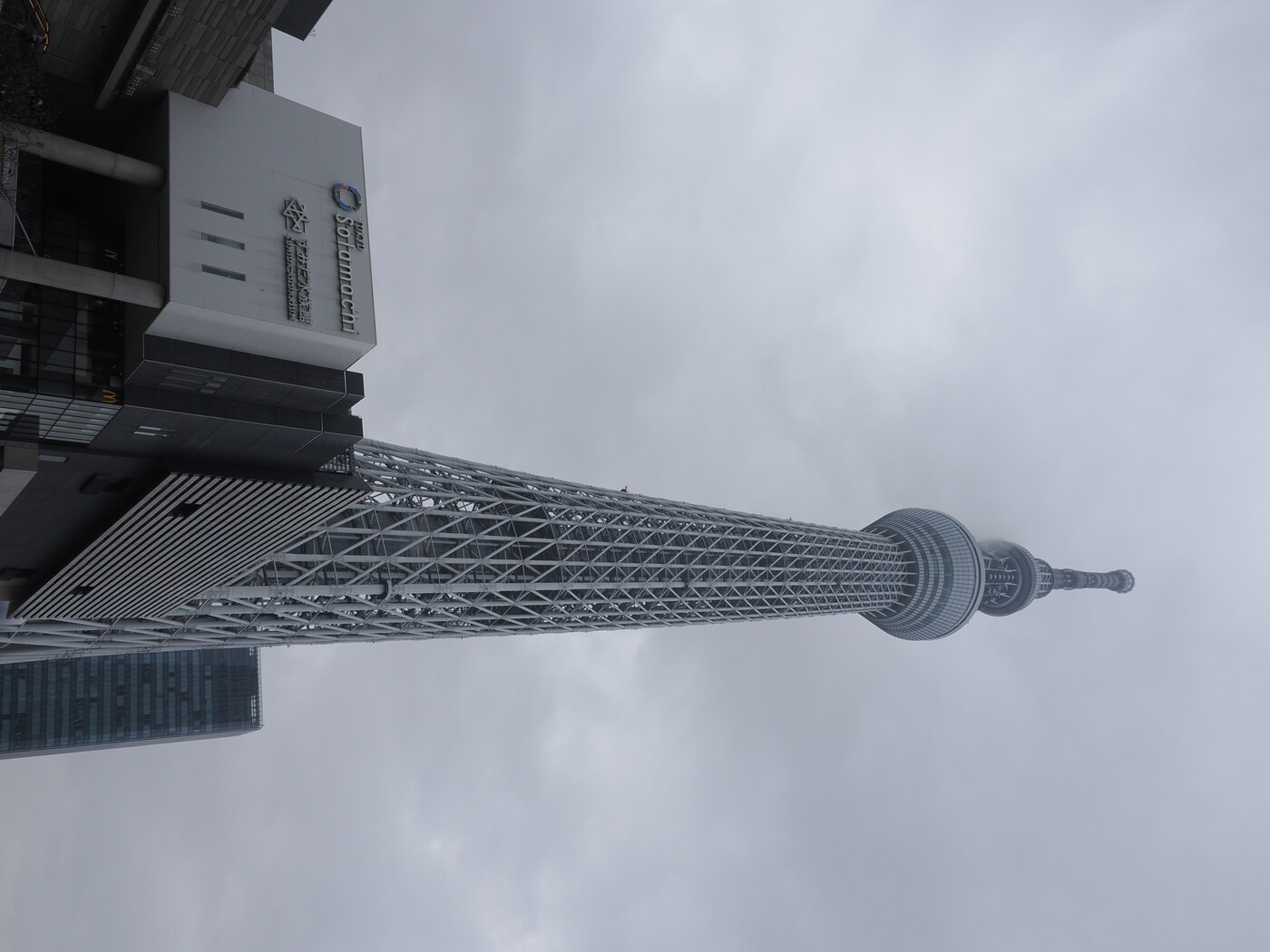 Tokyo Skytree od dołu — kratownica stalowa wchodzi w chmury, Solamachi po lewej