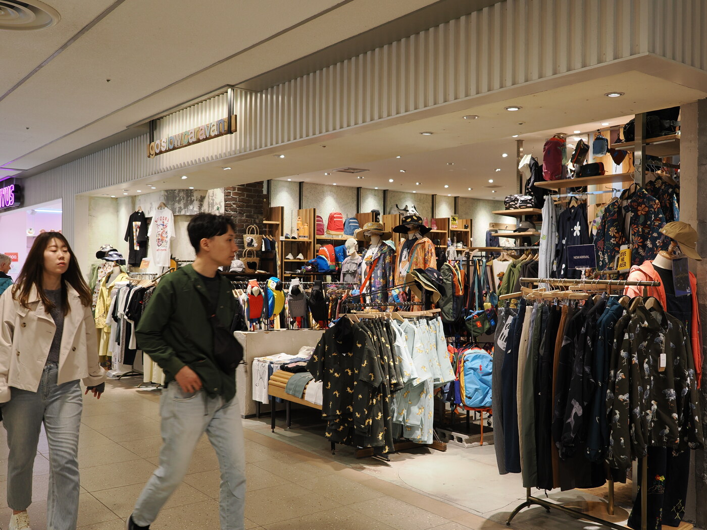 Go Slow Caravan — sklep z odzieżą casual i akcesoriami outdoorowymi w Solamachi, para przechodząca przed wejściem, kolekcja kapeluszy i koszul w kwiatowe wzory