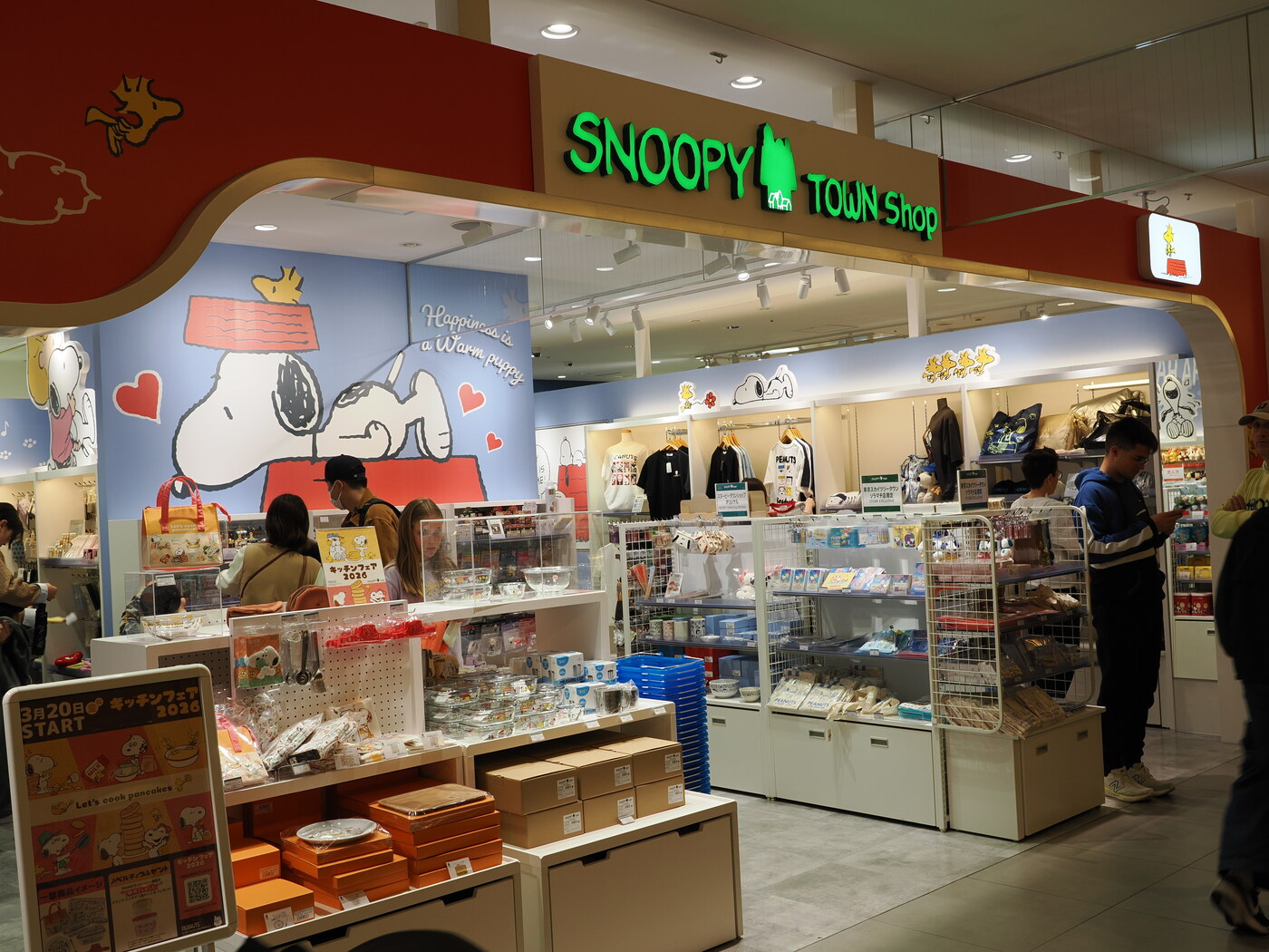 Snoopy Town Shop w Solamachi — kuchenny festiwal キッチンフェア 2026, szyld Szczęście to ciepły szczeniak, gabloty z naczyniami i gadżetami Peanuts