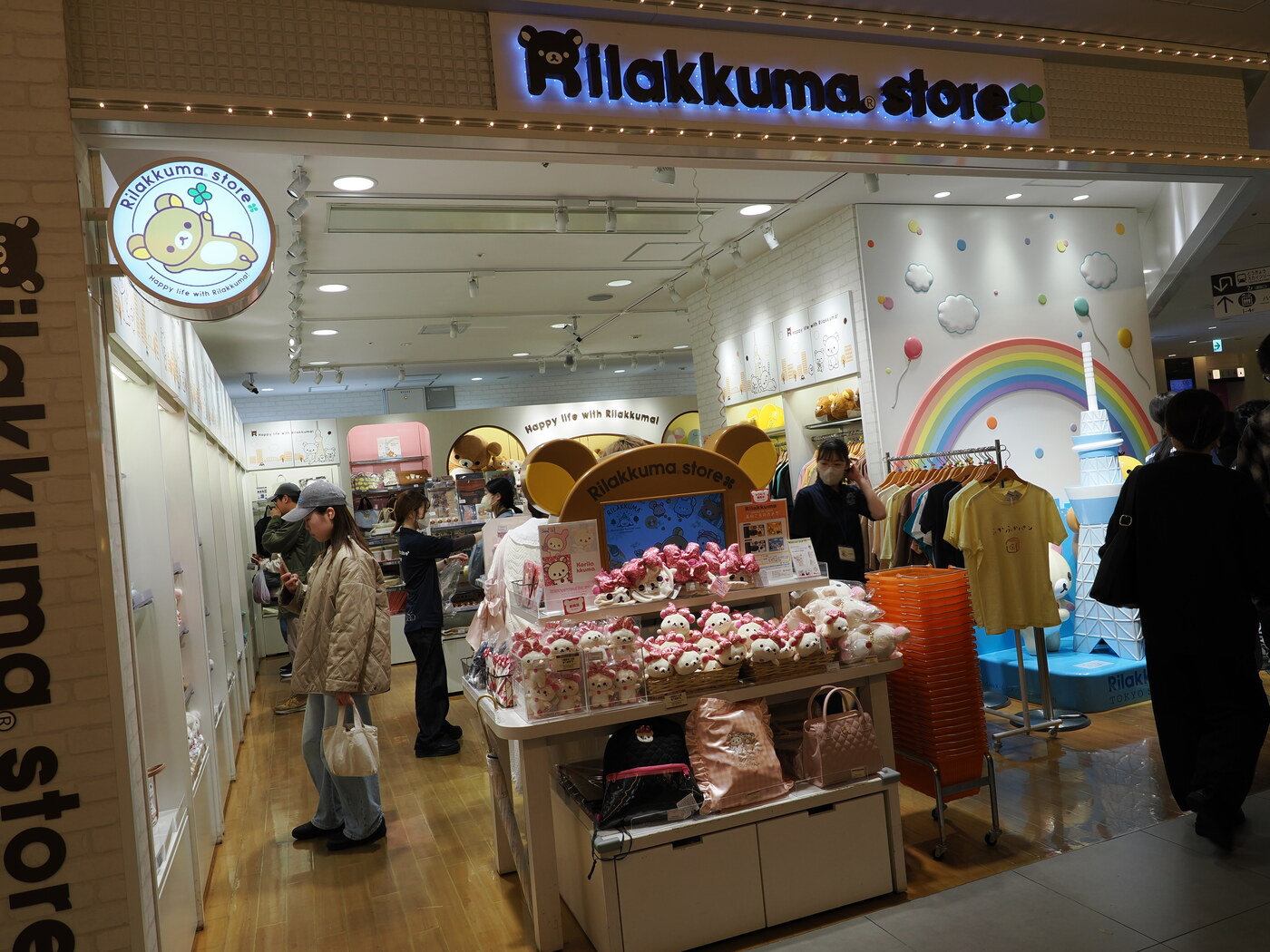 Rilakkuma Store w Solamachi — sklep San-X z misiem Rilakkuma, tęczowa ściana, stoisko z pluszakami Korilakkuma w różowych strojach, tłum kupujących