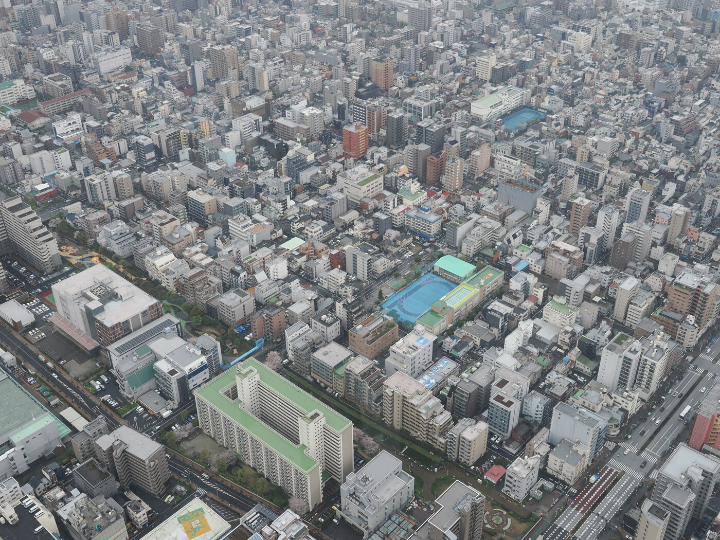 Tokio z wysokości 350m — gęsta zabudowa z boiskami szkolnymi z turkusowymi bieżniami, widoczna sieć ulic