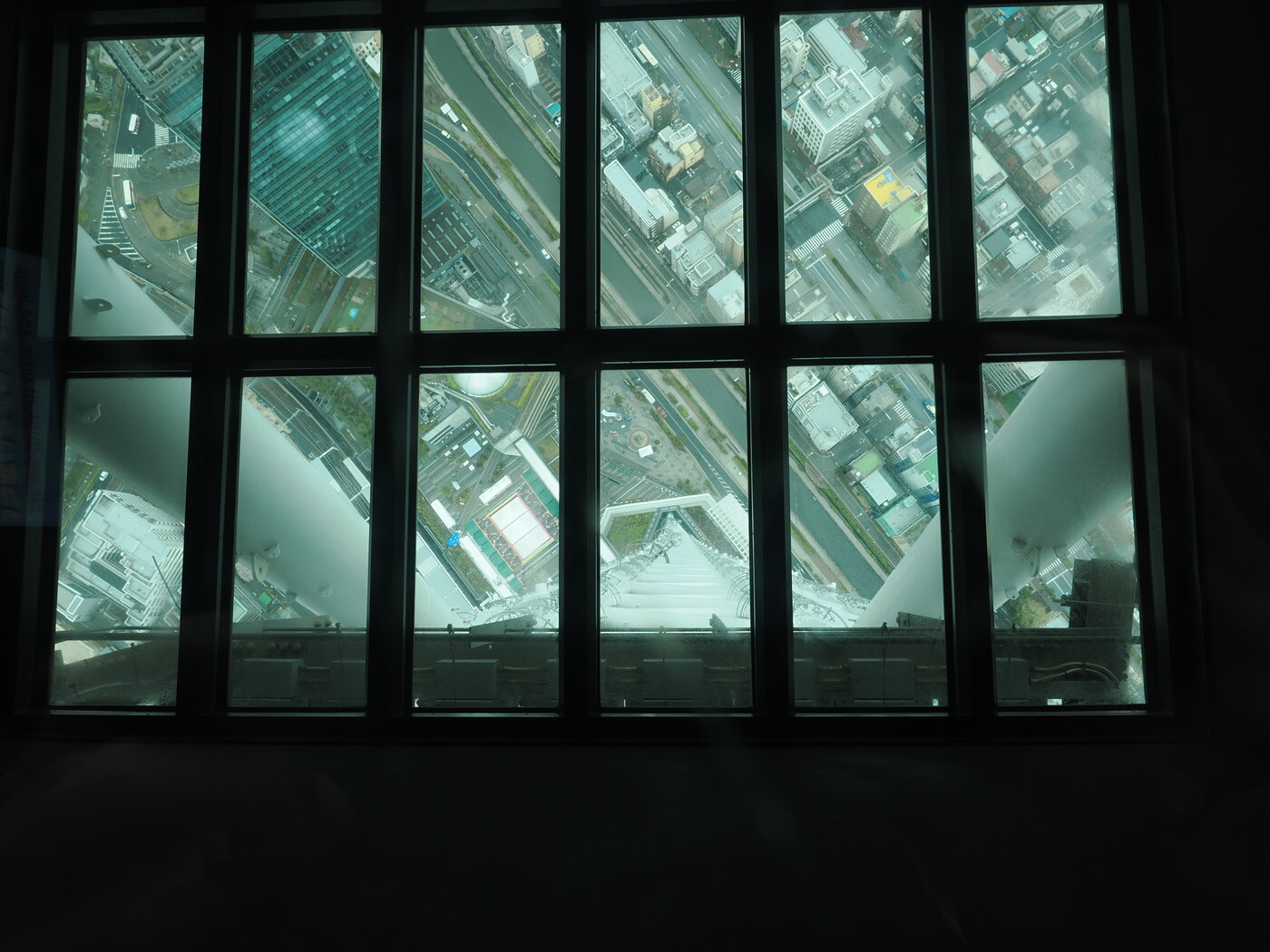 Szklana podłoga Tembo Galleria na 445m — widok w dół przez podłogę na zabudowę Tokio, ulice i kanały z 445 metrów, ciemne ramy ścian