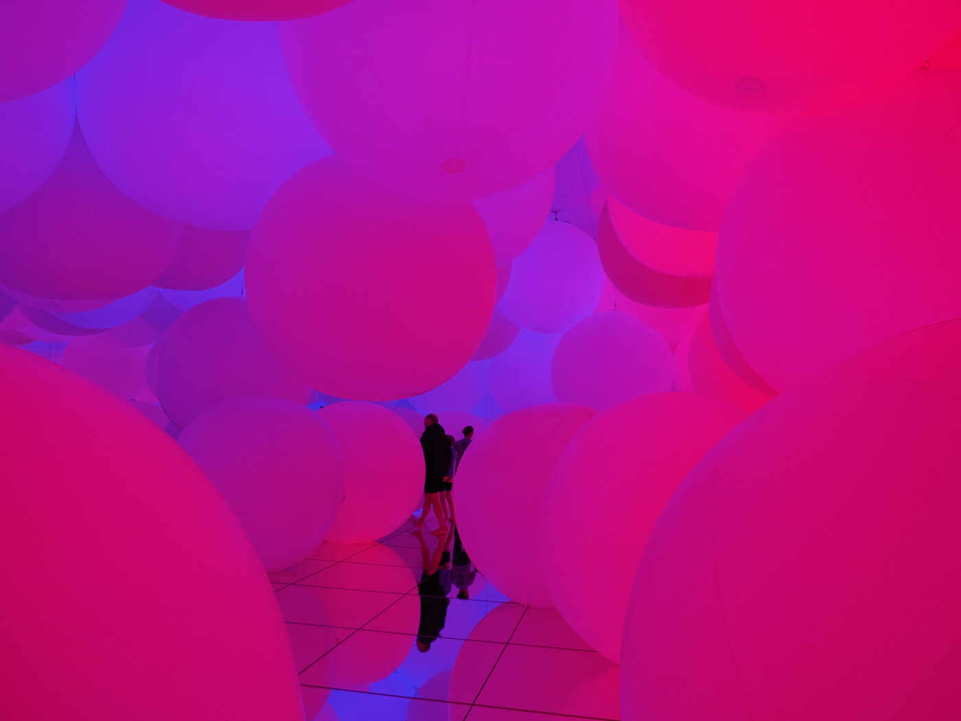 teamLab Planets — sala z wielkimi nadmuchanymi sferami oświetlonymi na różowo i niebiesko, dwie sylwetki między balonami, odbicie w lustrzanej podłodze