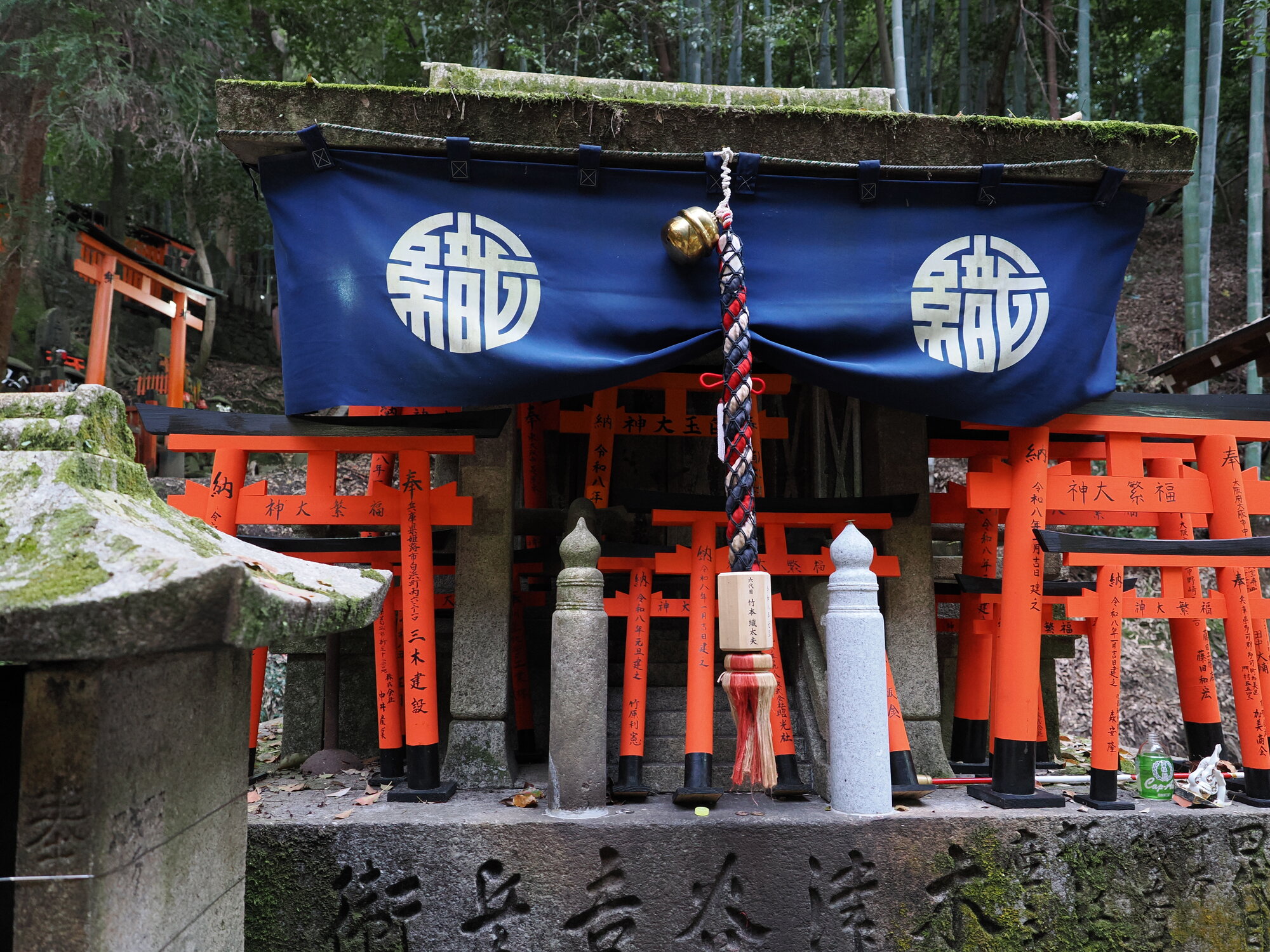 Mała kapliczka otsuka z niebieską kurtyną i miniaturowymi torii
