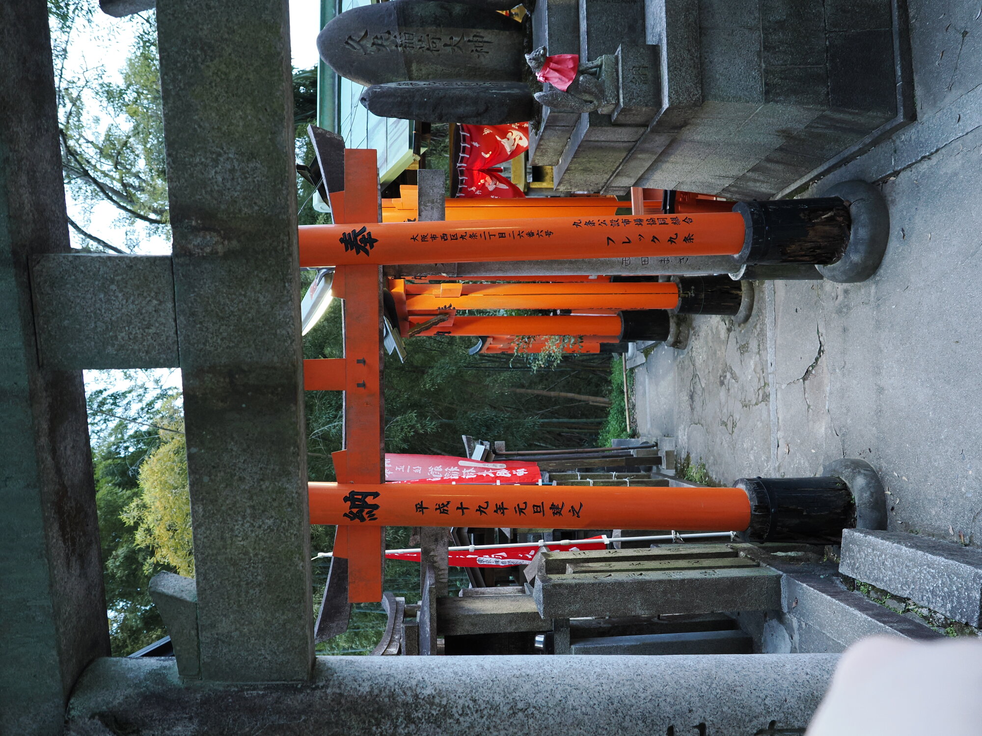 Przejście przez torii z stelą 稲荷大神 i figurką lisa w bambusowym lesie