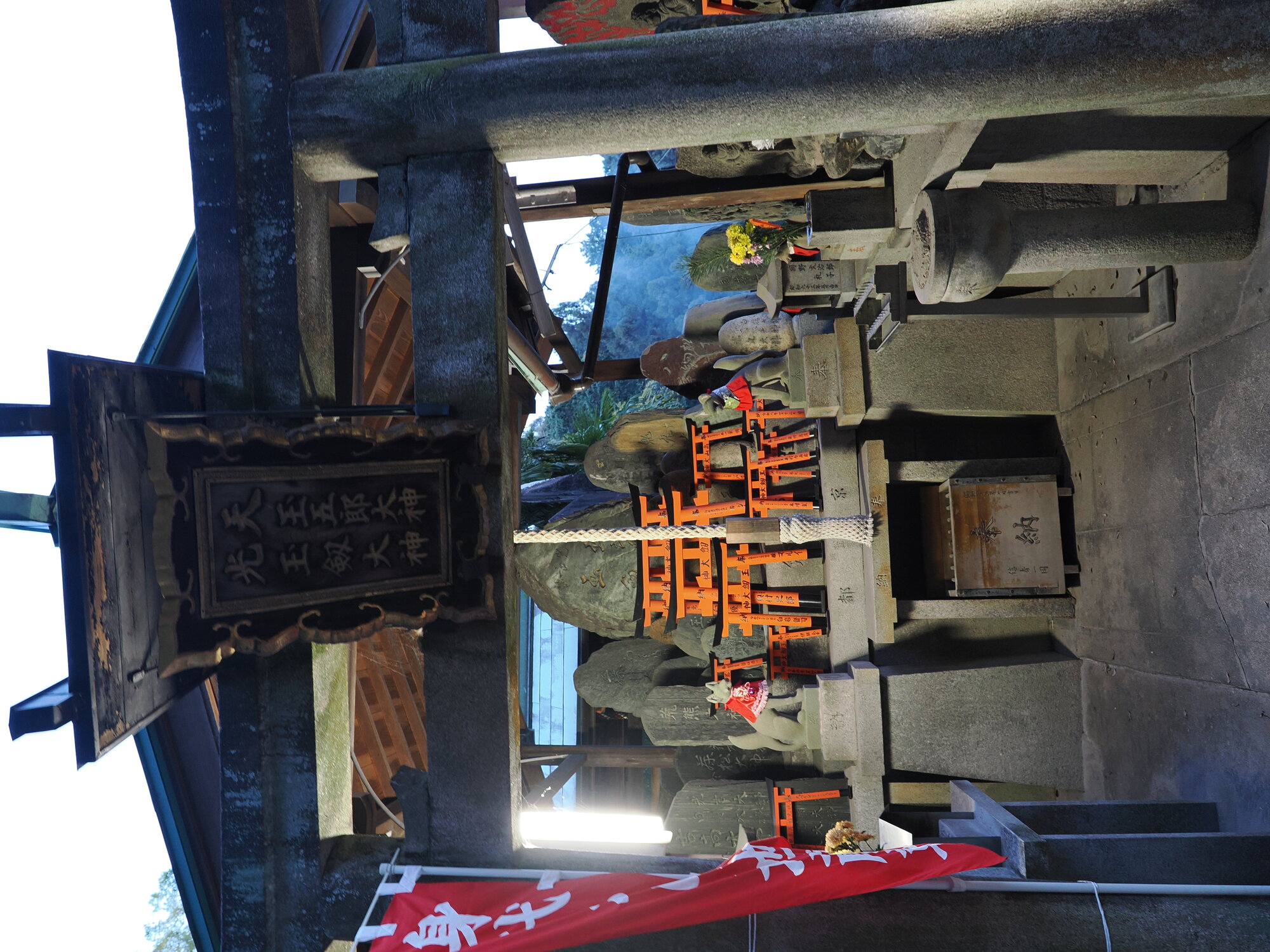 Kapliczka pod zadaszeniem z tablicą 天王五郎大神 i skrzynką na ofiary