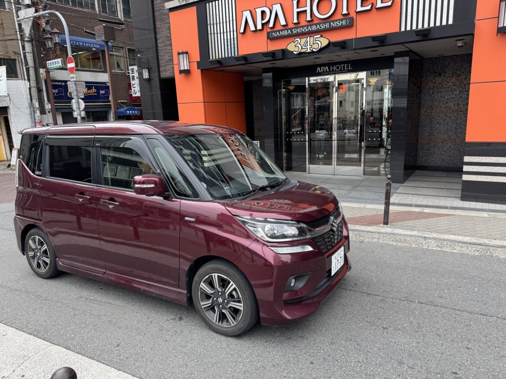 Bordowy kei-car Suzuki zaparkowany przed APA Hotel w wąskiej uliczce Namba