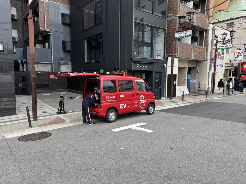 Elektryczny van Poczty Japońskiej EV z maskotką listonosza-misia przy 7-Eleven