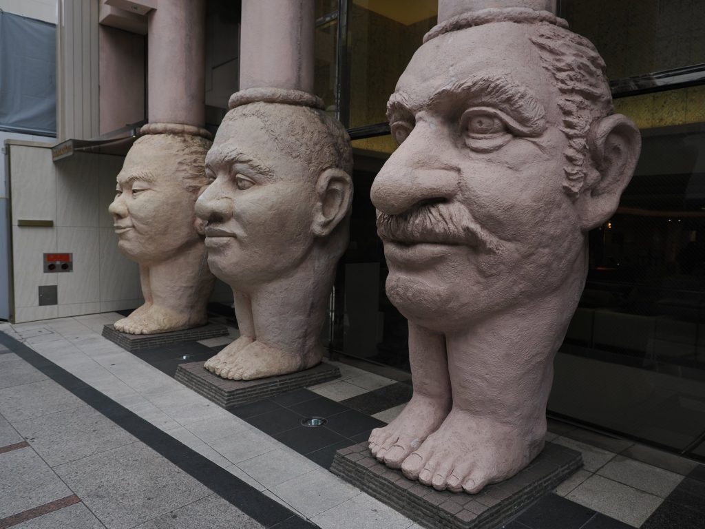 Trzy monumentalne rzeźby ludzkich głów na stopach przed budynkiem