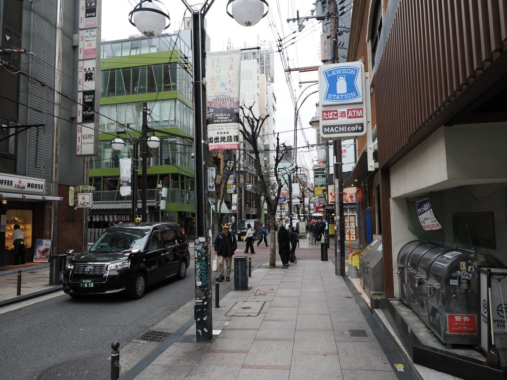 Ulica przy Dōtonbori z czarną taksówką Toyota JPN Taxi i szyldami