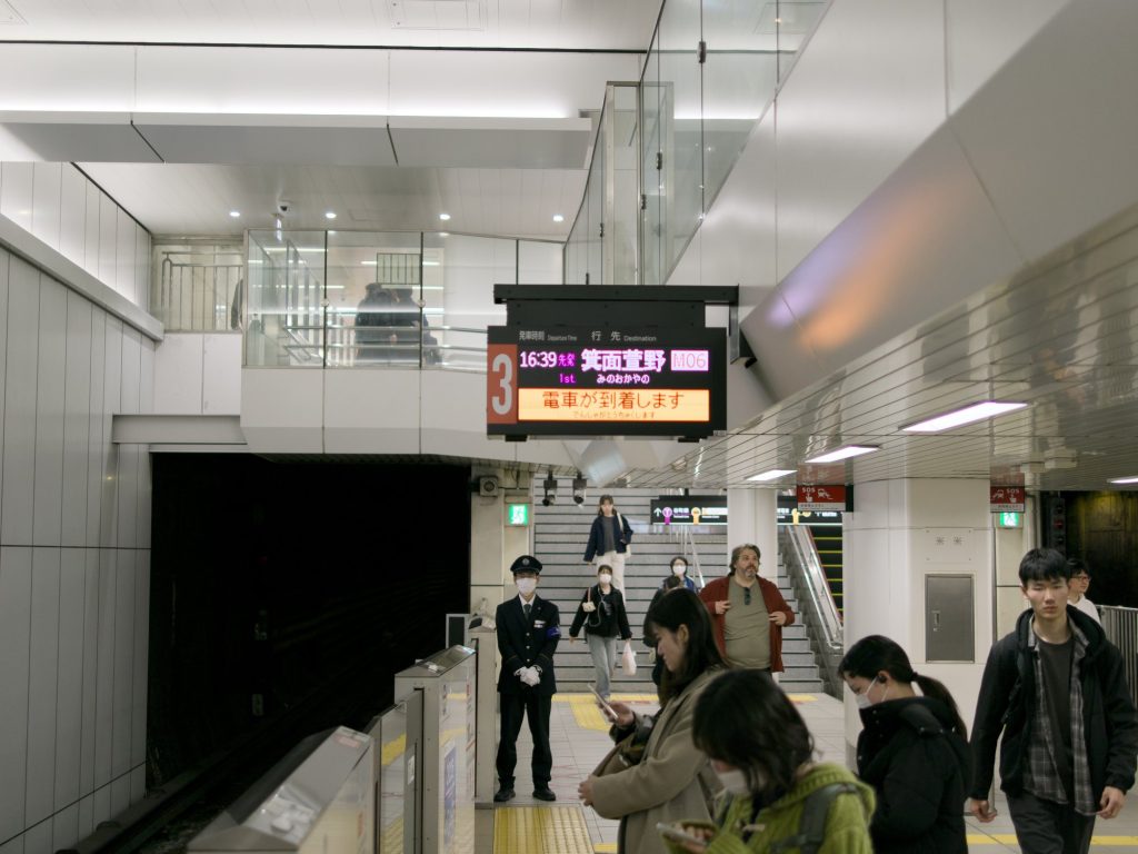 Peron metra Osaka z tablicą kierunku Minoo i pracownikiem