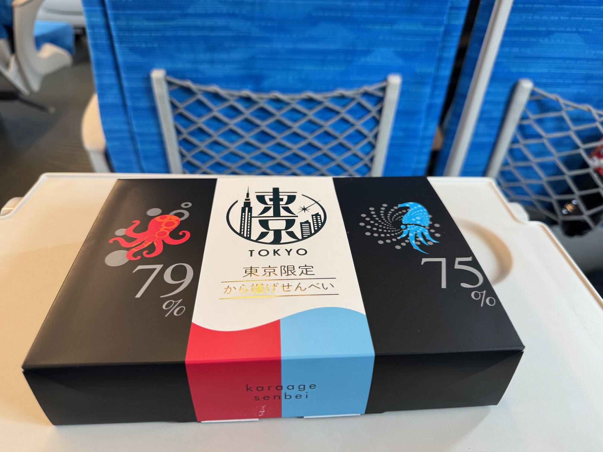 Pudełko karaage senbei z Tokio na stoliku Shinkansena — japońska przekąska na drogę, za oknem przelatują pola